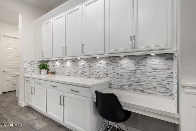 interior space with white cabinets, light tile patterned floors, light stone countertops, decorative backsplash, and built in desk