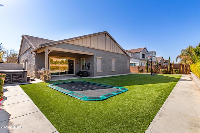 back of house featuring a hot tub, a lawn, and a trampoline