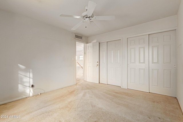 unfurnished bedroom with multiple closets, ceiling fan, and light carpet