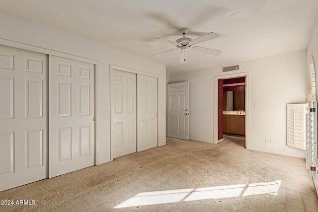 unfurnished bedroom featuring light carpet, ceiling fan, ensuite bathroom, and two closets