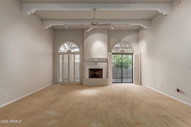 unfurnished living room with beamed ceiling, ceiling fan, light colored carpet, and rail lighting