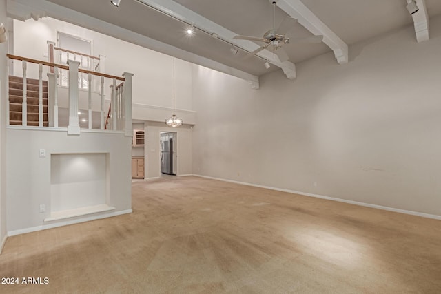 unfurnished living room featuring carpet, ceiling fan with notable chandelier, a towering ceiling, and beamed ceiling