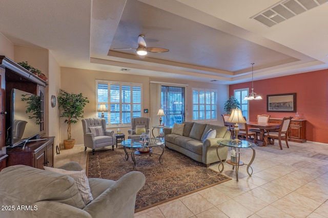 living room with a raised ceiling, a healthy amount of sunlight, light tile patterned floors, and ceiling fan with notable chandelier