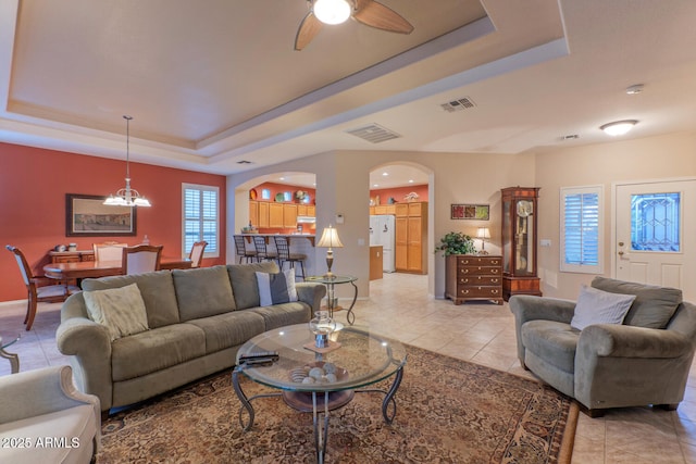 tiled living room featuring ceiling fan with notable chandelier and a tray ceiling