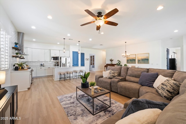living room with recessed lighting, light wood-style flooring, and ceiling fan with notable chandelier