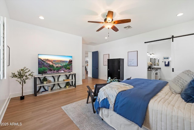 bedroom featuring light wood-type flooring, a barn door, baseboards, and recessed lighting
