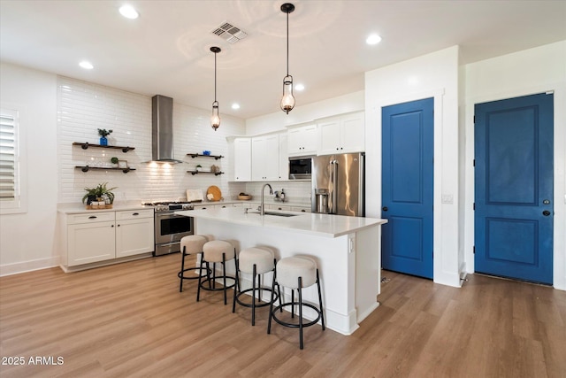 kitchen featuring visible vents, wall chimney range hood, a breakfast bar, high quality appliances, and a sink