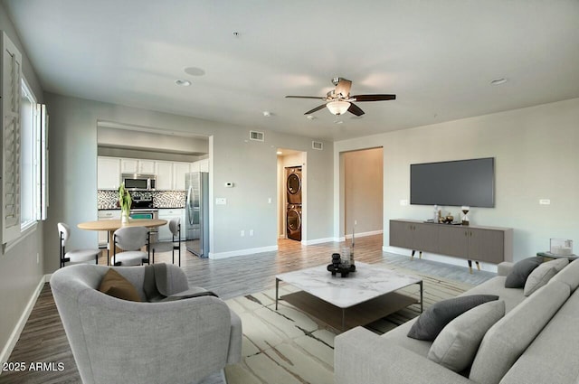 living room featuring light hardwood / wood-style floors, ceiling fan, and stacked washer and clothes dryer