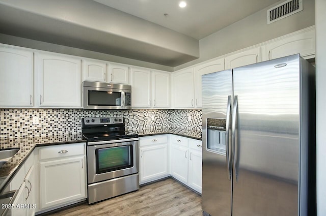 kitchen featuring white cabinets, light wood-type flooring, appliances with stainless steel finishes, and tasteful backsplash