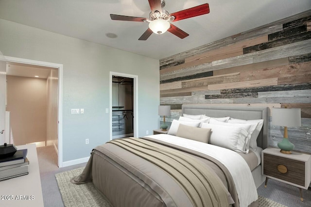 bedroom featuring wood walls, a walk in closet, ceiling fan, light colored carpet, and a closet