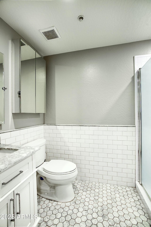 bathroom featuring vanity, a shower with door, tile patterned flooring, toilet, and tile walls