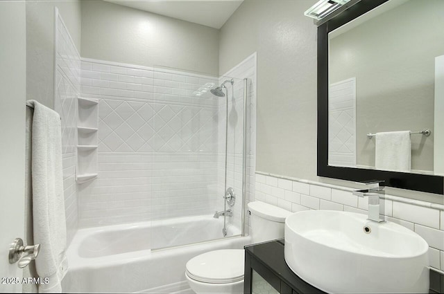 full bathroom with tiled shower / bath combo, toilet, sink, and tile walls