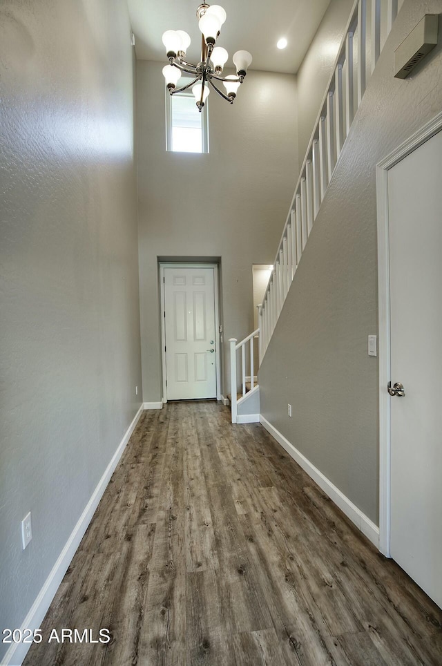 entryway with a chandelier, wood-type flooring, and a towering ceiling