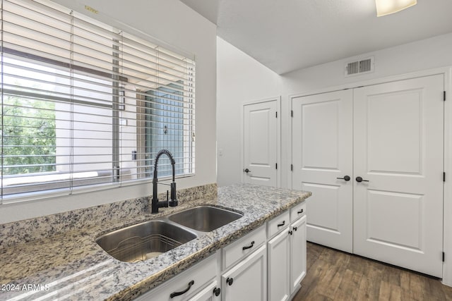 kitchen with light stone countertops, white cabinetry, dark wood-type flooring, and sink