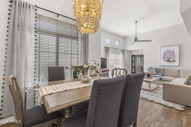 dining space featuring hardwood / wood-style flooring, ceiling fan with notable chandelier, and a towering ceiling