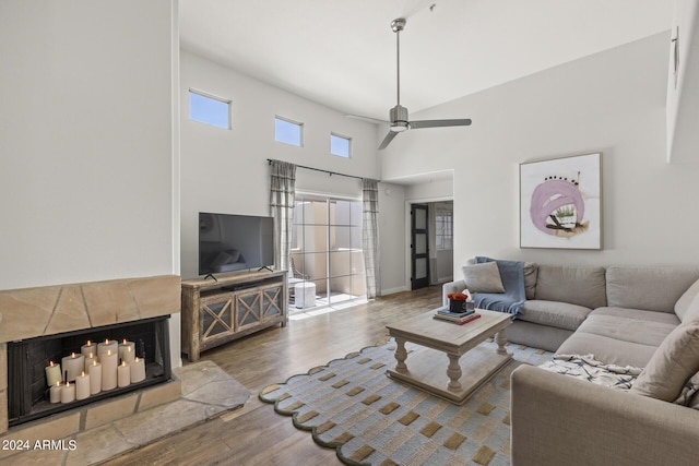 living room with a tile fireplace, ceiling fan, a towering ceiling, and hardwood / wood-style flooring