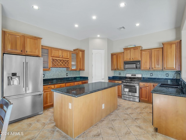 kitchen featuring sink, appliances with stainless steel finishes, dark stone counters, a kitchen island, and decorative backsplash