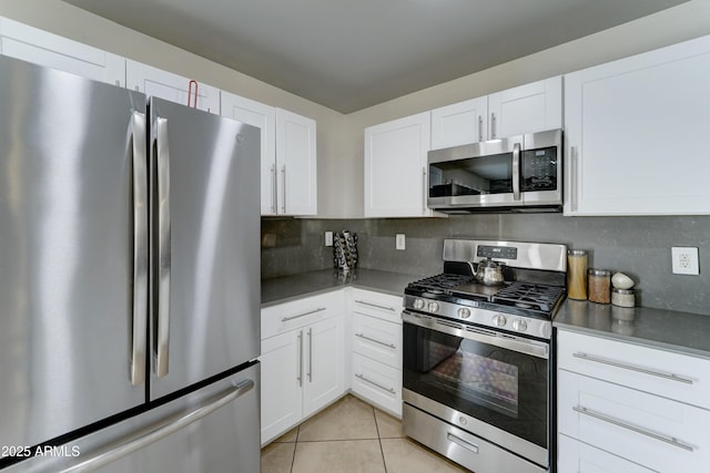 kitchen featuring light tile patterned floors, stainless steel appliances, dark countertops, decorative backsplash, and white cabinetry