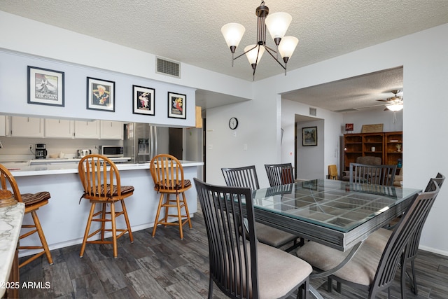 dining area with a textured ceiling, dark wood-style flooring, ceiling fan with notable chandelier, and visible vents