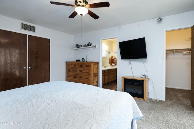 carpeted bedroom featuring baseboards, visible vents, connected bathroom, a ceiling fan, and a spacious closet