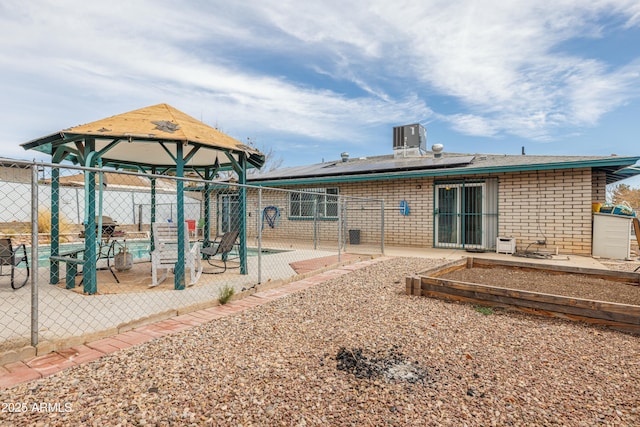 rear view of property with a patio, brick siding, a fenced backyard, and roof mounted solar panels