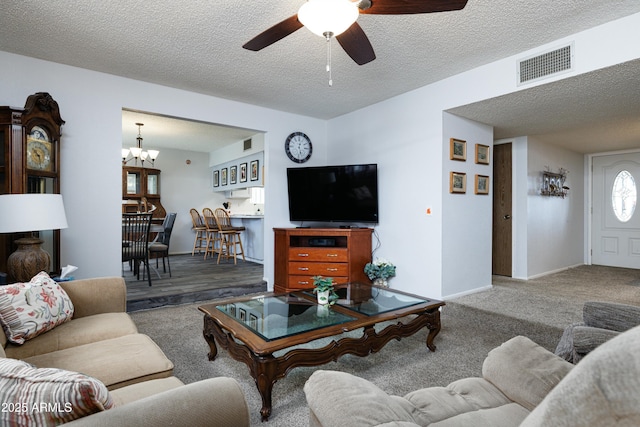 carpeted living area with baseboards, visible vents, a textured ceiling, and ceiling fan with notable chandelier