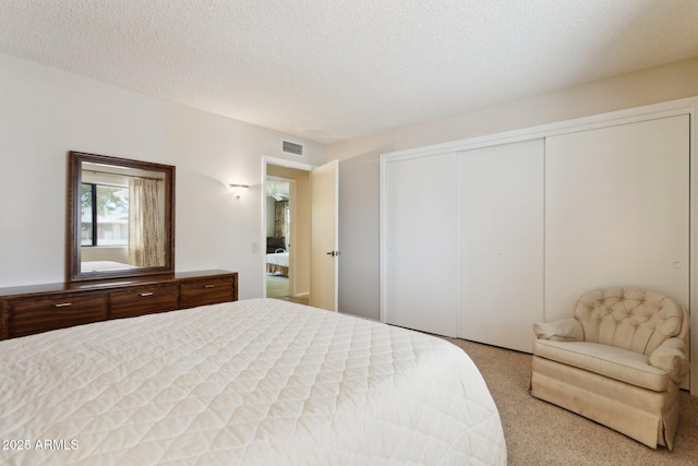 bedroom with a textured ceiling, visible vents, carpet, and a closet