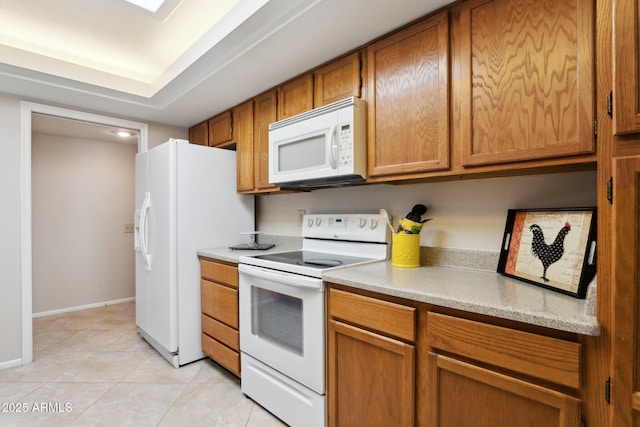 kitchen with light tile patterned flooring, white appliances, light countertops, brown cabinetry, and baseboards
