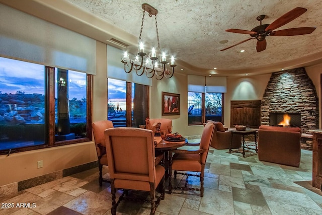 dining room with a stone fireplace, ceiling fan with notable chandelier, and a textured ceiling