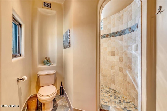 bathroom featuring toilet, tile patterned flooring, and a tile shower