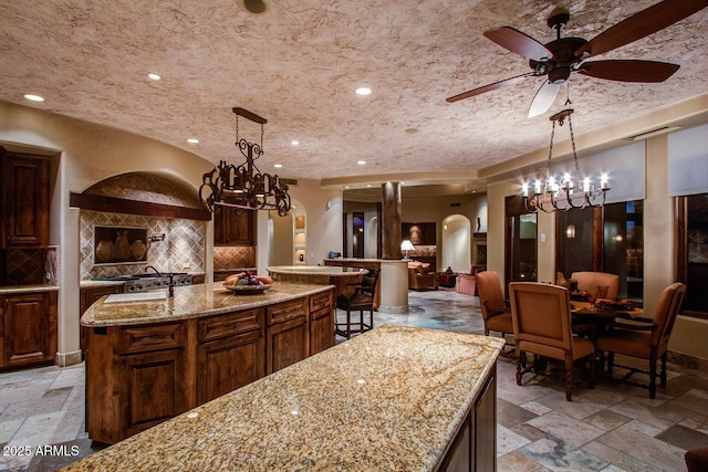 kitchen with a large island with sink, light stone countertops, pendant lighting, and decorative backsplash