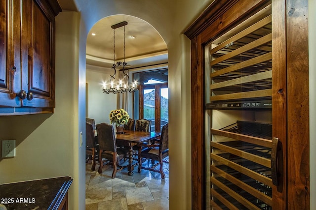 wine area featuring wine cooler, a raised ceiling, and a chandelier