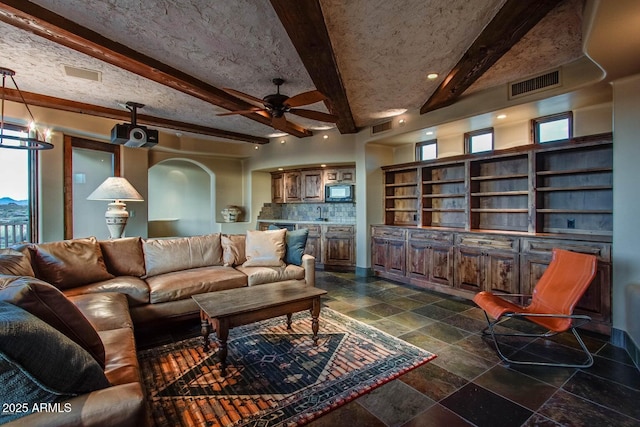 living room featuring ceiling fan, a textured ceiling, and beam ceiling