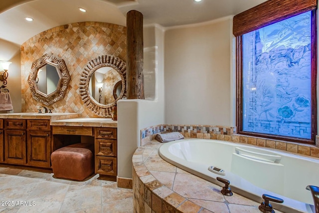 bathroom featuring a relaxing tiled tub, vanity, and backsplash