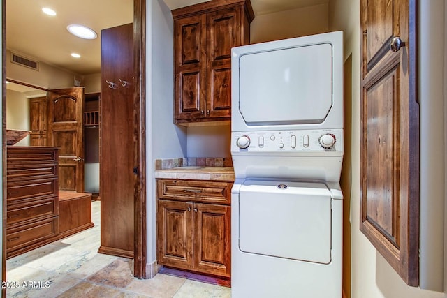 washroom featuring cabinets and stacked washer and clothes dryer