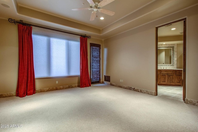 spare room with light carpet, a tray ceiling, and ceiling fan