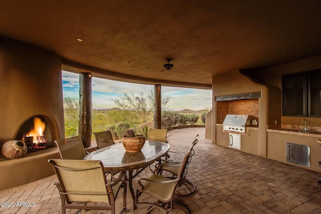 patio terrace at dusk with exterior fireplace, a grill, sink, exterior kitchen, and a mountain view