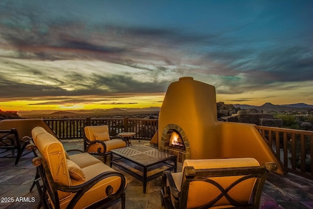 balcony at dusk with exterior fireplace, a mountain view, and a patio area