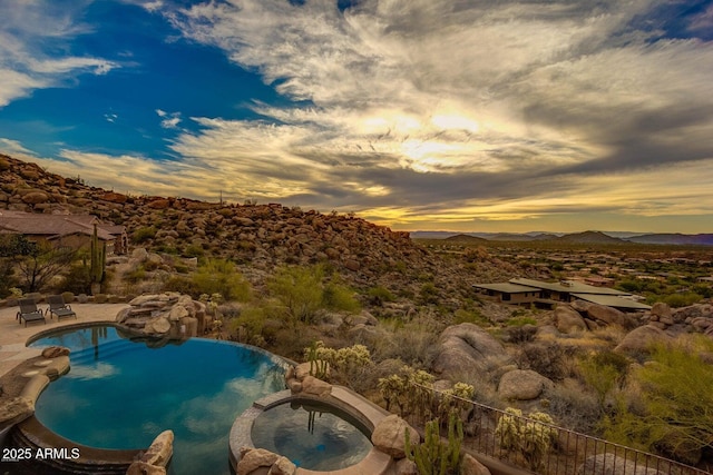 pool at dusk with an in ground hot tub and a mountain view