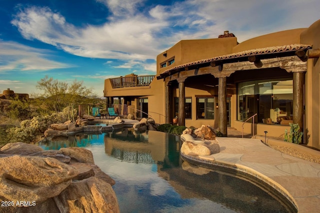 back of house featuring a swimming pool with hot tub, a patio, and a balcony