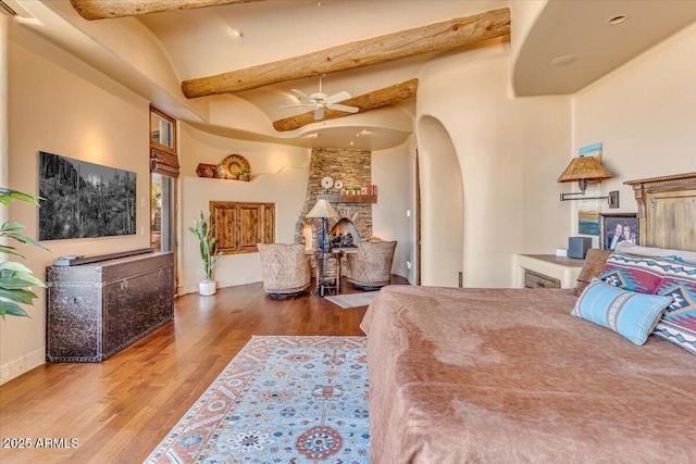 bedroom with hardwood / wood-style flooring, a stone fireplace, and lofted ceiling with beams