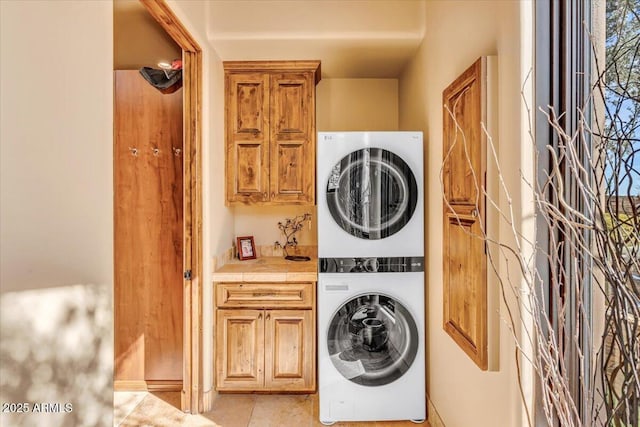 clothes washing area featuring cabinets and stacked washer and clothes dryer