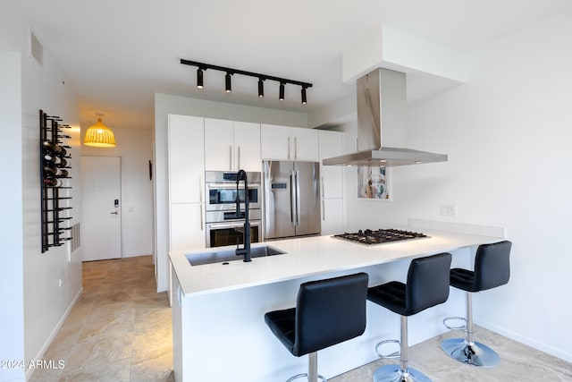 kitchen with island exhaust hood, kitchen peninsula, track lighting, stainless steel appliances, and white cabinetry