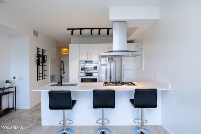 kitchen with kitchen peninsula, a kitchen breakfast bar, island range hood, and white cabinetry