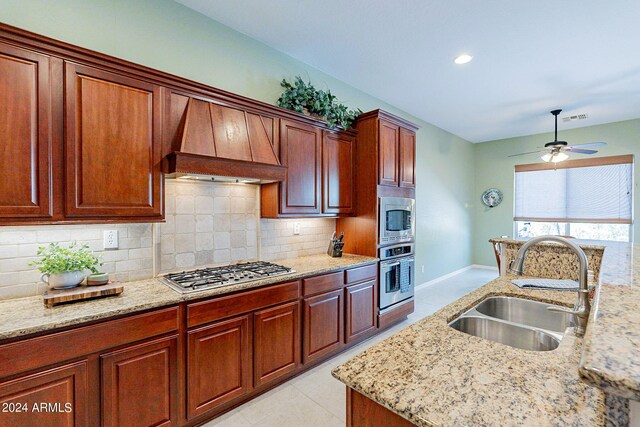 kitchen with a kitchen bar, light stone counters, an island with sink, custom range hood, and appliances with stainless steel finishes