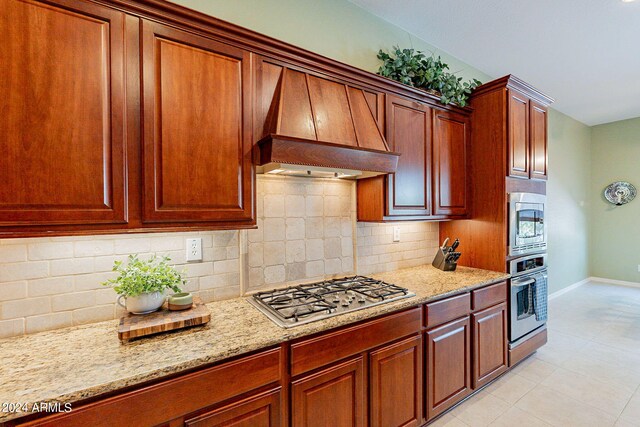 kitchen with sink, appliances with stainless steel finishes, light stone countertops, premium range hood, and decorative backsplash