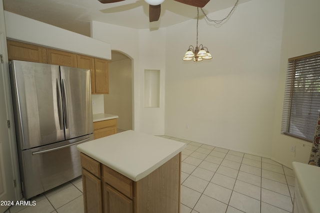 kitchen with ceiling fan with notable chandelier, light tile patterned floors, a kitchen island, stainless steel fridge, and pendant lighting