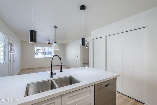 kitchen with sink, white cabinetry, hanging light fixtures, light hardwood / wood-style floors, and stainless steel dishwasher