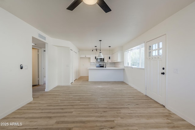 kitchen with white cabinetry, decorative backsplash, decorative light fixtures, kitchen peninsula, and light wood-type flooring