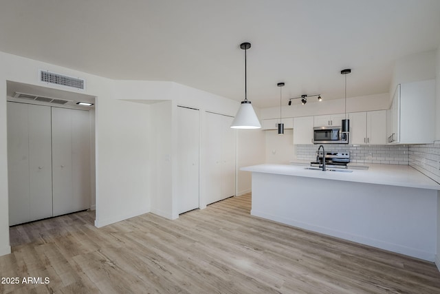 kitchen with appliances with stainless steel finishes, pendant lighting, white cabinets, backsplash, and kitchen peninsula